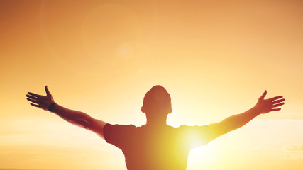 Young man standing outstretched at sunset. Bright solar glow and sky - obrazy, fototapety, plakaty