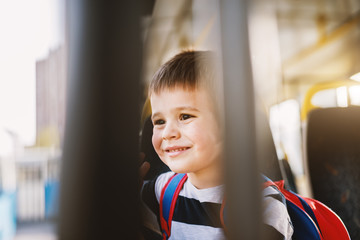 Small shy smiling boy is looking through the bus window.