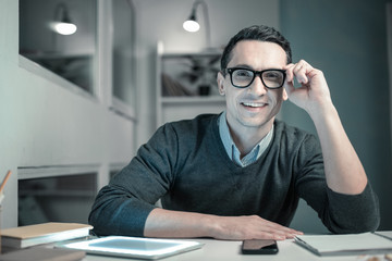 Office worker. Pleasant young smiling intern wearing glasses while working at office sitting at the table