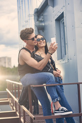 happy interracial couple listening music with earphones and taking selfie on smartphone on roof