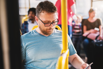 Serious mature man with glasses sitting in bus full of people and reading newspaper. © Dusan Petkovic