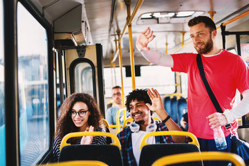 Young modern multicultural couple sitting in a public transportation and waiving to their friends outside.