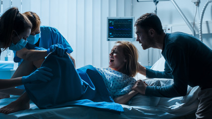 In the Hospital Woman in Labor Pushes to Give Birth, Obstetricians Assisting, Husband Holds Her Hand. Modern Delivery Ward with Professional Midwives. - obrazy, fototapety, plakaty