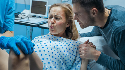 In the Hospital Close-up on Woman in Labor Pushes to Give Birth, Obstetricians Assisting, Husband Holds Her Hand. Modern Delivery Ward with Professional Midwives. - obrazy, fototapety, plakaty