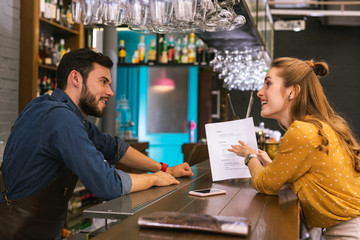 Checking the script. Young barman feeling interested while his active visitor showing him her new script for the play