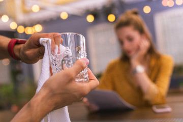 Transparent glass. Attentive experienced barman carefully holding a beautiful glass while cleaning it