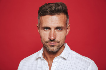 Portrait closeup of unshaved man 30s in white shirt looking at camera, isolated over red background