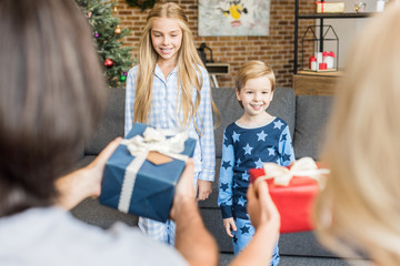 selective focus of parents presenting christmas gifts to happy children in pajamas