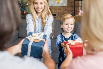 cropped shot of parents presenting christmas gifts to happy kids in pajamas