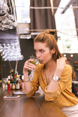 Drinking alcohol. Beautiful young girl thoughtfully drinking alcohol while sitting at the bar counter