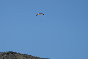 Fototapeta na wymiar Paraglider with rainbow canopy gliding over the mountainside