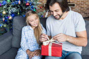 Fototapeta na wymiar cute smiling daughter in pajamas looking at happy father opening christmas present