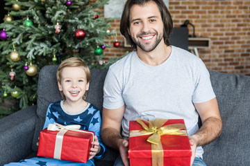 Obraz na płótnie Canvas happy father and cute little son in pajamas holding christmas gifts and smiling at camera