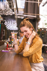 Feeling shy. Beautiful relaxed young woman sitting at the bar counter and smiling while drinking alcohol