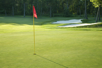 Obraz premium Golf green with red flag in late afternoon sunlight