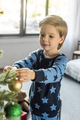 cute smiling little boy in pajamas decorating christmas tree