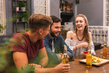 Good friends. Cheerful young girl laughing while sitting in the bar with her best friends