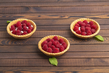 Raspberry tartlets with cream and mint on wooden background