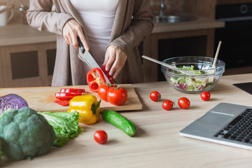 Woman cooking healthy salad and using laptop at home