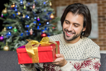 handsome happy man holding christmas present at home