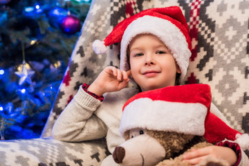 cute little boy in santa hat holding teddy bear and smiling at camera at christmas time
