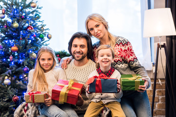 happy family in sweaters holding christmas presents and smiling at camera