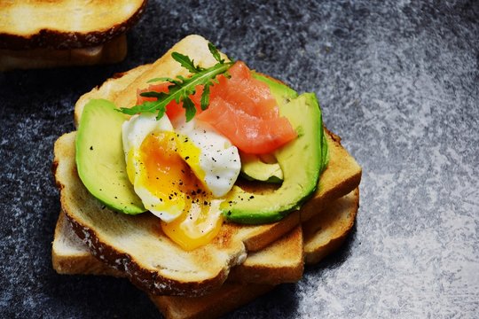 Poached egg toast isolated. Breakfast tost with poached egg, avocado and salmon on the black background