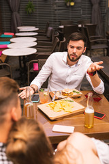 Stop this. Expressive young man asking his friends to sop hugging while sitting in the bar with them