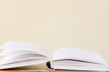 Opened book lying on wooden table blank white wall background. College school university education learning literacy concept. Poster banner with copy space