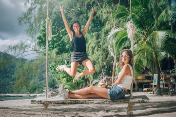 Two beautiful girlfriend enjoy a swing and drink coconut