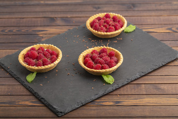 Tartlet with cream and fresh raspberries, served on a slate plate.