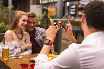Smile. Calm young man holding modern smartphone and taking photos of his friends