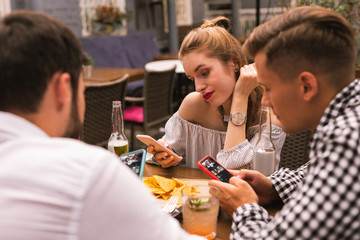 Looking at screens. Young of modern generation thoughtfully looking at the screens of devices while sitting at the table