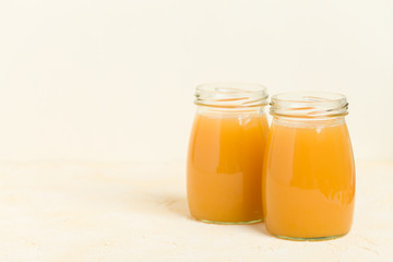 Peach smoothie in glass jars on yellow pastel background.