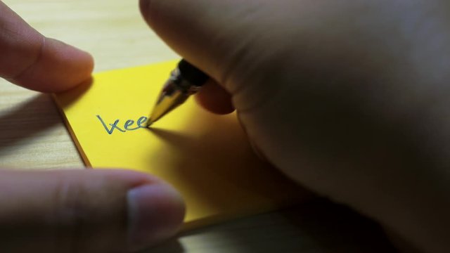 Men writing a keep going on a paper note with a blue pen and soft focus scene.