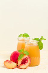 Peach smoothie in glass jars with fresh ripe fruits and green mint leaves on yellow pastel background.