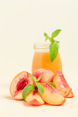 Peach smoothie in glass jars with fresh ripe fruits and green mint leaves on yellow pastel background.