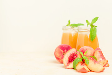 Peach smoothie in glass jars with fresh ripe fruits and green mint leaves on yellow pastel background.