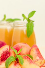 Peach smoothie in glass jars with fresh ripe fruits and green mint leaves on yellow pastel background.