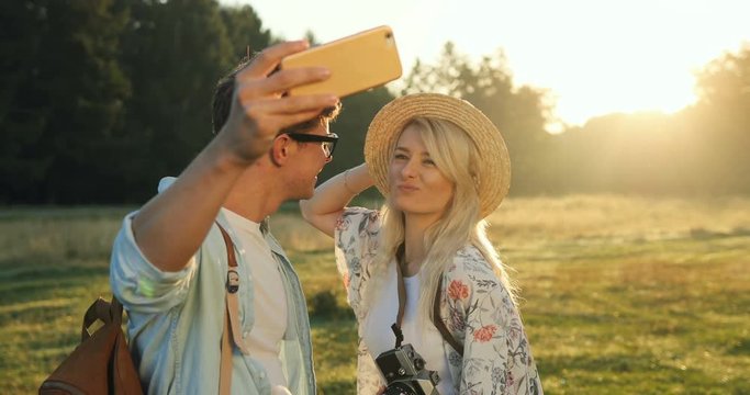 Close up of the joyful young boyfriend and girlfriend taking nice selfie photos on the smartphone camera and kissing in the beautiful nature in the field.