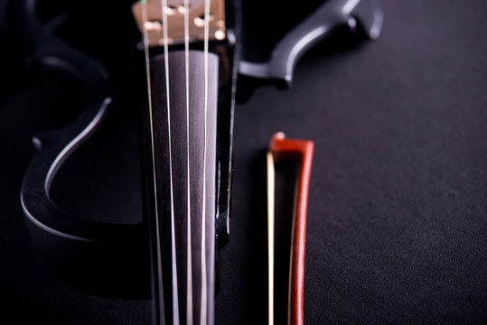 Beautiful black electric violin lying  on a black background