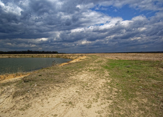 sandy shore of the pond against the stormy sky