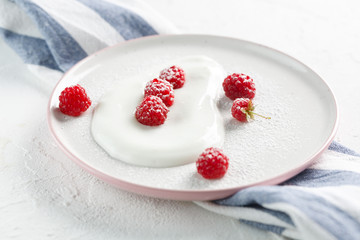 plate with homemade yogurt and ripe raspberries with on white table