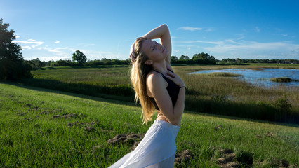 young blonde woman posing against the wind in landscape with peaceful face during sunset skirt & hair blown by the wind