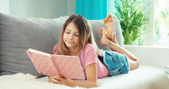 Teen girl lying on sofa with notebook reading it