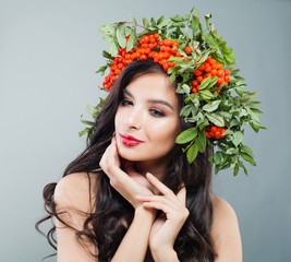 Young woman brunette with long wavy hair, makeup and autumn berries and leaves wreath