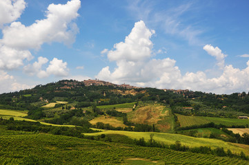 Obraz premium Distant town on top of a hill during a beautiful sunny day over big green fields.