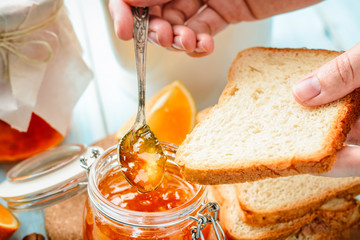 female hand smears toasts with homemade orange jam