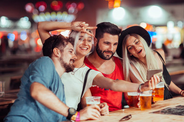 Group of friends drinking beer and taking selfie at music festival 