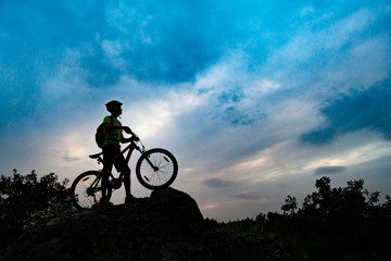 Silhouette of Cyclist with Mountain Bike on Rock at Sunset. Extreme Sports and Enduro Cycling Concept.